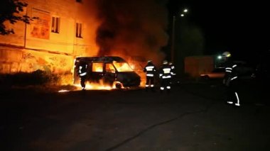 A car is burning and gasoline is dripping and burning. Unrecognizable firefighter spraying water and foam for extinguishing the fire. Loopable seamless animation cinemagraph