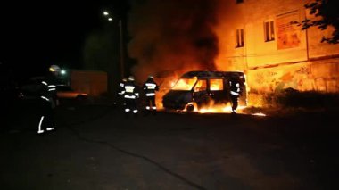 A car is burning and gasoline is dripping and burning. Unrecognizable firefighter spraying water and foam for extinguishing the fire. Loopable seamless animation cinemagraph