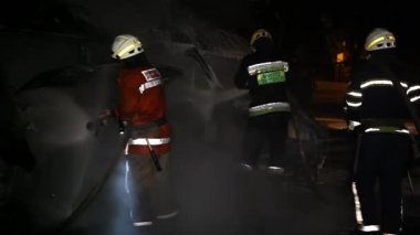 A car is burning and gasoline is dripping and burning. Unrecognizable firefighter spraying water and foam for extinguishing the fire. Loopable seamless animation cinemagraph