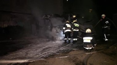 A car is burning and gasoline is dripping and burning. Unrecognizable firefighter spraying water and foam for extinguishing the fire. Loopable seamless animation cinemagraph