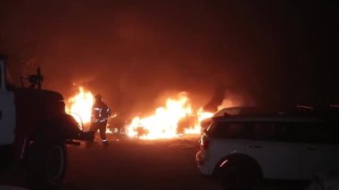 Şehir caddesinde yangın söndürücüyle yangını söndürmeye çalışan ama içerisi tamamen yanmış bir araba yangını.