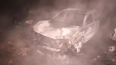 Şehir caddesinde yangın söndürücüyle yangını söndürmeye çalışan ama içerisi tamamen yanmış bir araba yangını.