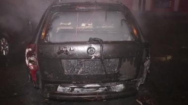 Şehir caddesinde yangın söndürücüyle yangını söndürmeye çalışan ama içerisi tamamen yanmış bir araba yangını.