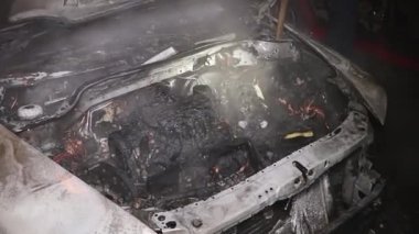 Şehir caddesinde yangın söndürücüyle yangını söndürmeye çalışan ama içerisi tamamen yanmış bir araba yangını.