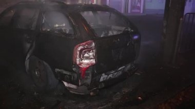 Şehir caddesinde yangın söndürücüyle yangını söndürmeye çalışan ama içerisi tamamen yanmış bir araba yangını.