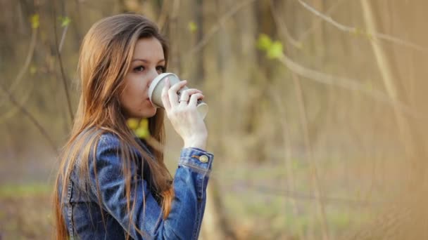 Mujer joven bebe una bebida caliente de una taza de papel — Vídeos de Stock