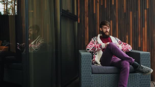 Bebaarde man maakt gebruik van een telefoon zit in een stoel — Stockvideo