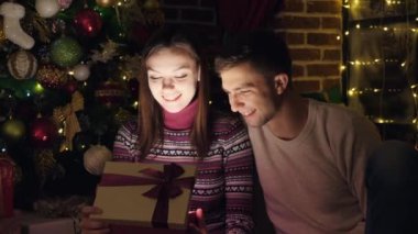 Bir Noel hediyesi. Bir erkek ve bir kadın bir kutu bir hediye ile açın. Parlak ışık kutusu. Noel, yeni yıl.