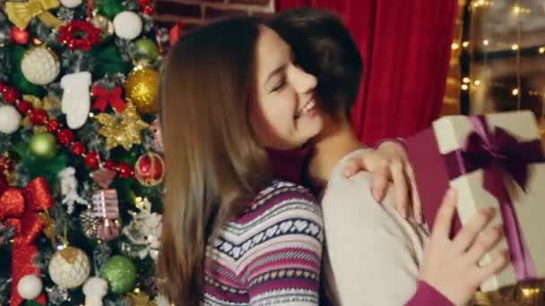 彼の美しい恋人にクリスマス プレゼントを与えます バック グラウンドで飾られたクリスマス ツリー — ストック動画