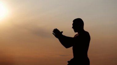 Bir sporcunun silueti gün batımında tek başına nefes alma egzersizi yapar, gün batımında meditasyon yapar.