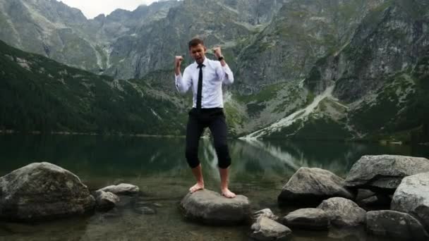 Empresário bem sucedido feliz da vitória, emoções felizes loucas e dançando perto de um lago nas montanhas ao pôr do sol — Vídeo de Stock