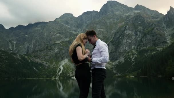 Homme en costume fait une demande en mariage à sa femme bien-aimée près d'un lac de montagne, met sur une bague de fiançailles — Video