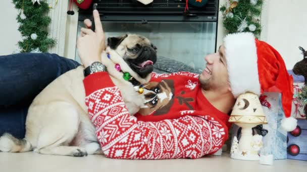 Uomo abbraccio divertente cane carlino in costume di Natale indossa il cappello di Babbo Natale e utilizzare il telefono cellulare, Capodanno e Natale — Video Stock