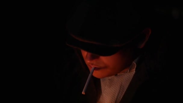 Крупный план человека, детектива или бандита в плоской кепке зажигает сигарету от спички в темноте — стоковое видео