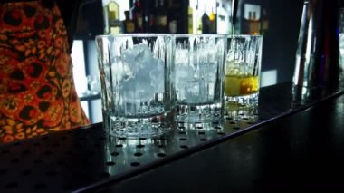 Gece kulübünde barın üstünde buz olan bir bardağa viski döken barmene yakın plan.