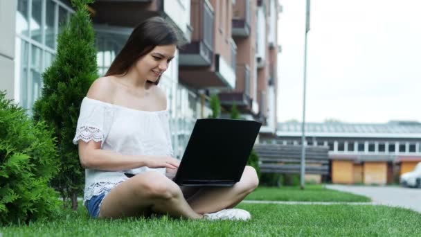 Счастливая студентка работает на ноутбуке в кампусе, сидя на траве — стоковое видео