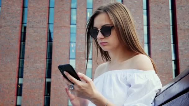 Mujer segura de usar el teléfono móvil en la calle, edificio de ladrillos modernos — Vídeo de stock