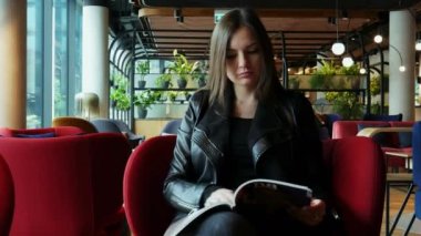 Güzel bir kadın modern bir kafede beklerken dergi okur.