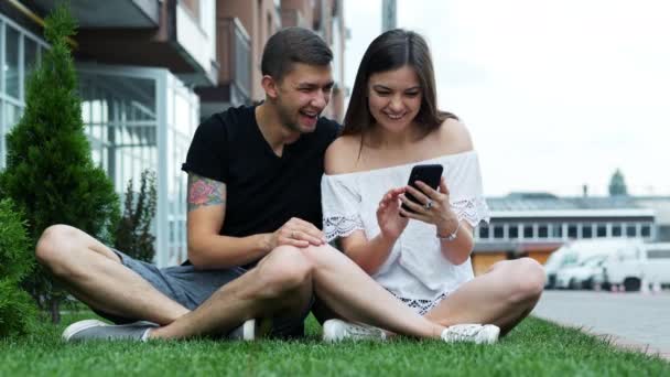 Casal feliz usando um telefone celular enquanto sentado na grama, compras on-line, surf — Vídeo de Stock