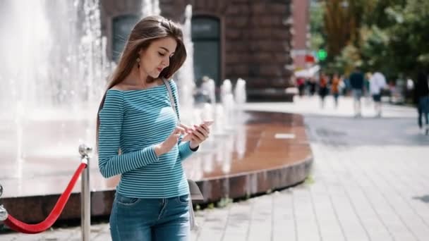 Giovane, ragazza alla moda utilizza uno smartphone su una strada della città, una donna stampa un messaggio, chiacchierando — Video Stock