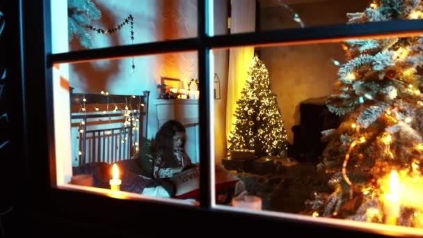 Съемка через окно, маленькая девочка написать письмо Санте возле елки в постели, Рождество и Новый год — стоковое видео