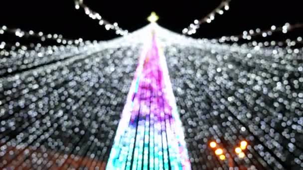 Wazig achtergrond van bloemenslingers lichten op kerstboom in de stad — Stockvideo