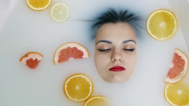 Közelkép egy gyönyörű nő arcáról a tejfürdőben, tele gyümölccsel, — Stock videók