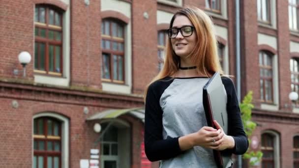Retrato de cerca de una estudiante o freelancer, mujer con gafas de pie con portátil y mirando a la cámara — Vídeos de Stock