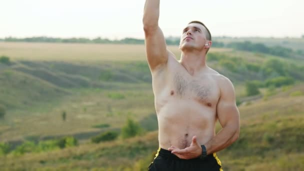 El hombre fuerte hace un ejercicio de respiración solo al atardecer, meditando al atardecer — Vídeos de Stock