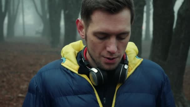 Άνδρας αθλητής βάζει ασύρματα ακουστικά σε ένα πάρκο της πόλης, κρύο ομιχλώδες πρωί — Αρχείο Βίντεο