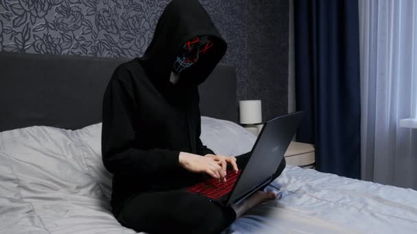 Hackerin in schwarzer Maske und Kapuzenpulli am Laptop im Schlafzimmer, Hackerin — Stockvideo