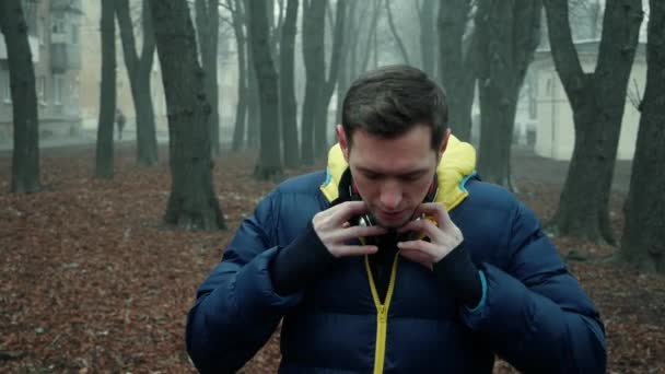 Atleta masculino coloca fones de ouvido sem fio em um parque da cidade, manhã nebulosa fria — Vídeo de Stock