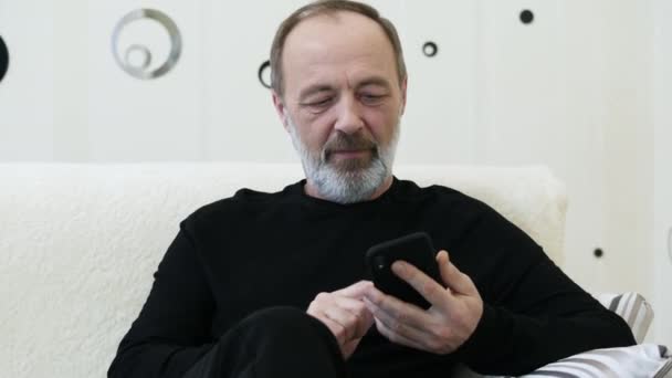 Homem de meia-idade com barba cinza usa o telefone em casa, close-up — Vídeo de Stock