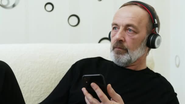 Portret van de man van middelbare leeftijd in draadloze hoofdtelefoon geniet van muziek, zoeken naar nieuwe muziek in het internet op mobiele telefoon — Stockvideo