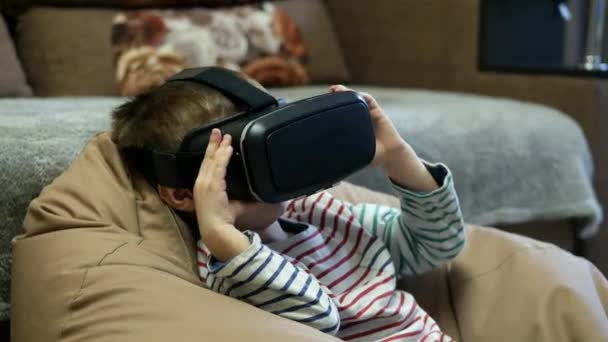 Child wearing virtual reality glasses and watching vr video at home at soft chair bag — 图库视频影像