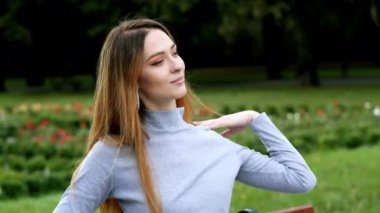 Close-up portrait of attractive smiling modern redhead woman puts on glasses and looking at camera at park