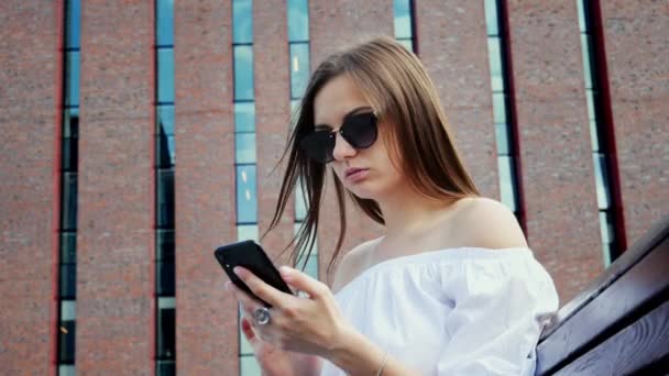 Modern young woman use mobile phone on the street, modern bricks building — Stock video