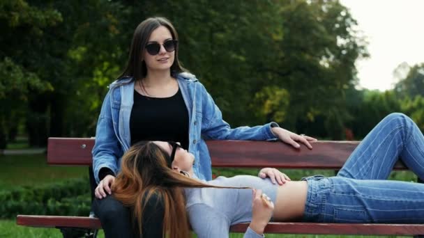 Οι φιλενάδες ξεκουράζονται στο παγκάκι στο πάρκο. Δύο γυναίκες κουτσομπολιά. — Αρχείο Βίντεο