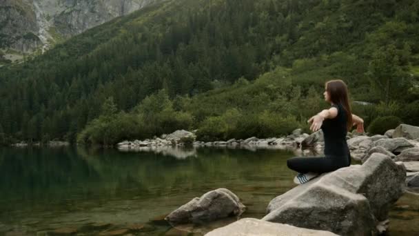 Mujer joven hermosa y saludable medita en un lago de bosque en las montañas — Vídeo de stock