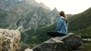 Genç turist kadın bir dağ gölünde dinleniyor, yüksek dağlarda manzaranın tadını çıkarıyor..