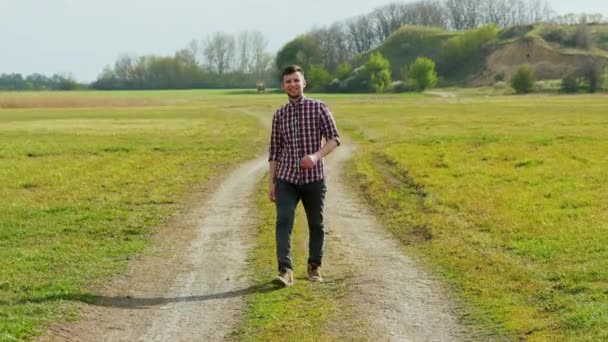 Happy hipster guy marche dans le champ au coucher du soleil, sourit, se sent libre . — Video
