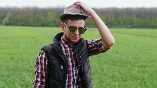Funny portrait of cool farmer puts on a hat in the green wheat field — Stock Video