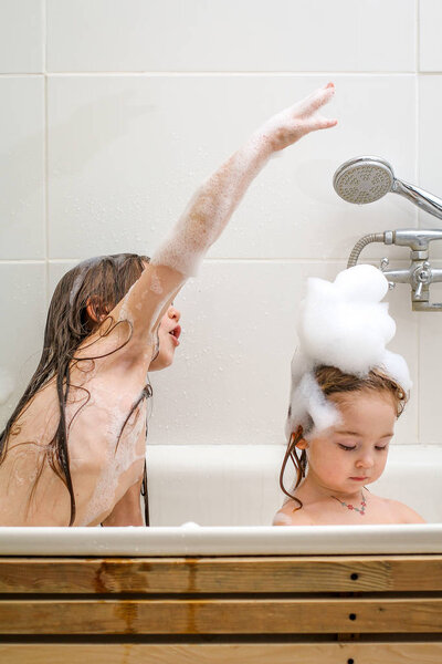 Two little sisters play in a bath.