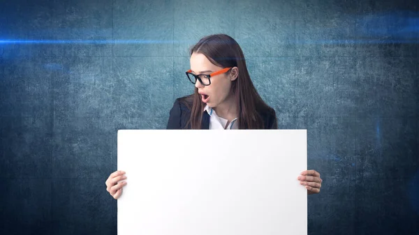 Retrato de mulher de negócios surpreso com placa branca em branco em azul isolado. Modelo feminino com cabelo comprido em óculos . — Fotografia de Stock