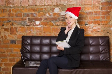Noel Baba kız iş kadını ile defter ve laptop deri kanepede elbiseli loft ofisinde. İş kavramı.