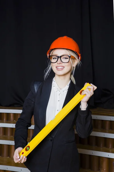 Beautiful blonde businesswoman with application tier at loft office in orange construction helmet and suit.