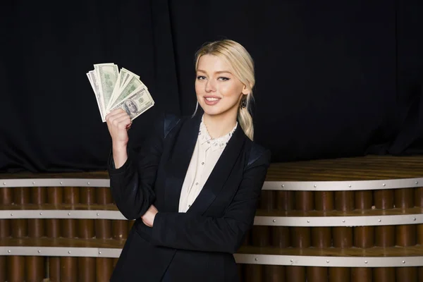 Όμορφη ξανθιά επιχειρηματίας με χρήματα στο πατάρι γραφείο σε μαύρο κοστούμι. — Φωτογραφία Αρχείου