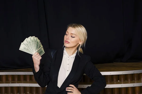 Beautiful blonde businesswoman with money at loft office in black suit. — Stock Photo, Image