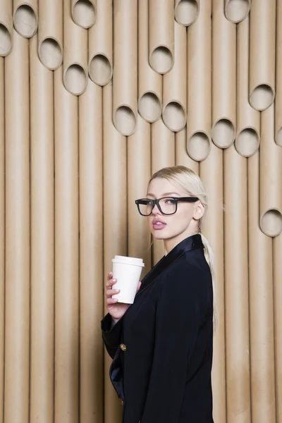 Hermosa mujer de negocios rubia sorprendida en vestido negro y gafas con taza de café . — Foto de Stock