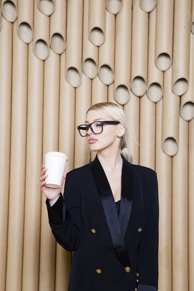 Hermosa mujer de negocios rubia sorprendida en vestido negro y gafas con taza de café . —  Fotos de Stock